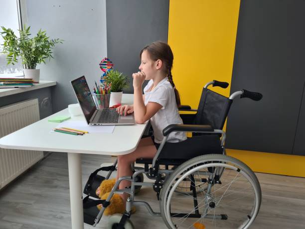 Teenage girl child in a wheelchair with a laptop indoors. Distance learning and education